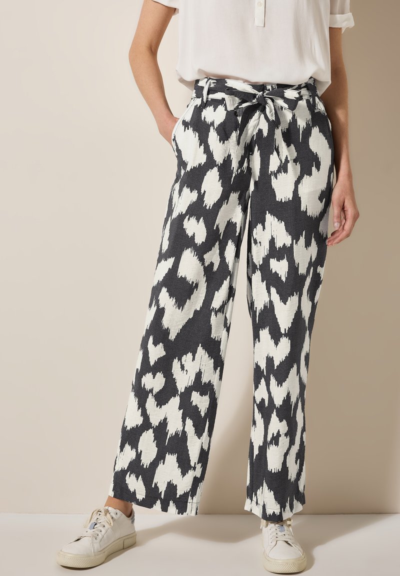 Pantaloni larghi a righe in bianco e nero con vita regolabile, realizzati in tessuto strutturato e dotati di tasche laterali, abbinati a sneaker bianche.