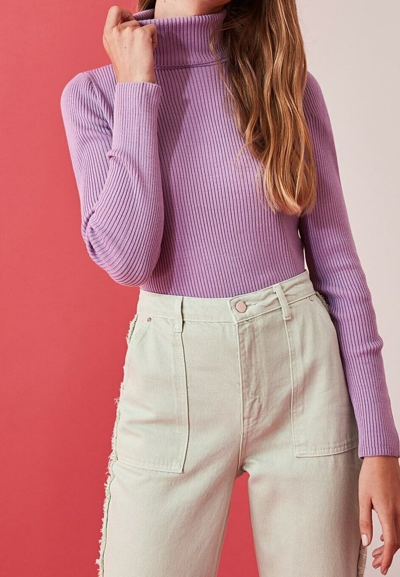 Haut à col roulé à manches longues en maille côtelée couleur lavande, associé à un jean en denim vert clair taille haute avec des accents latéraux et des poches avant.