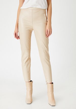 Beige læderbukser med en slim fit, der har sidelommer og lynlåse ved anklerne. Glat tekstur med subtile syningsdetaljer.