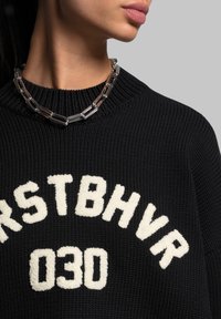 Black knitted sweater with white fluffy lettering "FIRSTBHV 030" and a silver chain necklace. Close-up view of design and texture.