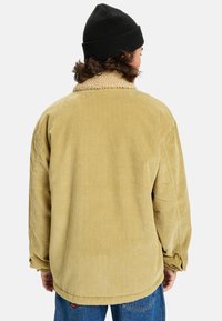 Giacca di velluto corduroy giallo pallido con colletto in shearling, maniche lunghe e una vestibilità rilassata, caratterizzata da una texture a coste verticali.