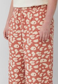 Lichte koraalkleurige broek met een crèmekleurig dierenprint, elastische tailleband met een drawstring, en een ontspannen pasvorm, van opzij weergegeven.