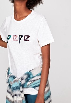 Weißes Baumwoll-T-Shirt mit rundem Ausschnitt, verziert mit einem bunten, mit Perlen besetzten "PEPE"-Design. Ein blau-grau-weiß gestreifter Schal ist um die Taille gewickelt.