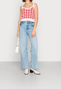 Červený a bílý úpletový top s vzorem psa zubatého spojený se světle modrými džínami s širokými nohavicemi a bočními rozparky, doplněný bílými kotníkovými botami s blokovým podpatkem.