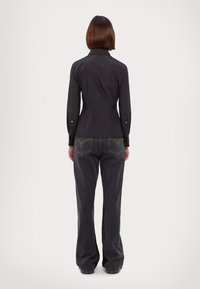 Camicia nera con colletto e maniche lunghe, design aderente. Abbinata a jeans grigi scuri a campana con cuciture gialle sui taschini posteriori.