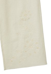 Tessuto in lino di un beige chiaro con ricami floreali intricati. Il design presenta dettagli con elementi ritagliati e cuciture sottili.