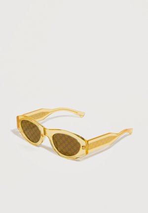 Rumene prosojne sončna očala v mačjem slogu z rjavimi lečami, na belem ozadju z vzorcem zveznih logotipov Gucci.