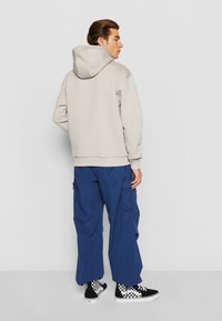 Haut gris clair avec capuche à cordon, associé à un pantalon cargo bleu marine doté de poches et des baskets basses à carreaux noir et blanc.