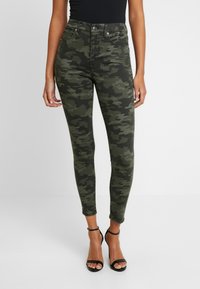 Jeans ajustados de talle alto con estampado de camuflaje en tonos verdes oscuros y textura suave. Cuenta con bolsillos frontales y cierre de botón en la parte delantera.