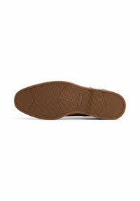 Semelle en caoutchouc marron avec un motif texturé, dotée de rainures circulaires et horizontales pour une meilleure adhérence. La marque ALDO est visible sur le côté.