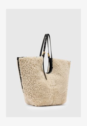 Kangaskassi, jossa on pörröinen kermaisen värinen villapinta ja sileät mustat nahkakoristeet. Varustettu säädettävin mustin olkahihnoin ja tilavalla muotoilulla.