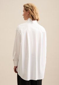 Witte oversized blouse met een hoge kraag, knoopmanchetten en een gladde textuur. Heeft een rechte achternaad en een gebogen zoom.