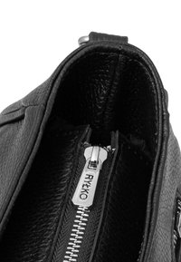 Interno di una borsa a tracolla in pelle nera che mostra un compartimento con zip e hardware argentato, con rivestimento testurizzato che ne migliora la durabilità e il design.