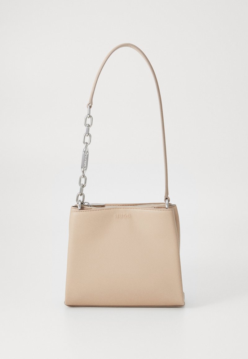 Sac à main en cuir beige au toucher lisse, avec une accent en chaîne argentée sur la poignée et une fermeture éclair. "HUGO" embouti à l'avant.
