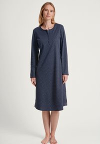 Camicione a maniche lunghe di colore blu scuro con pois bianchi. Presenta un collo rotondo e una fila di bottoni. Tessuto morbido con fessure laterali.