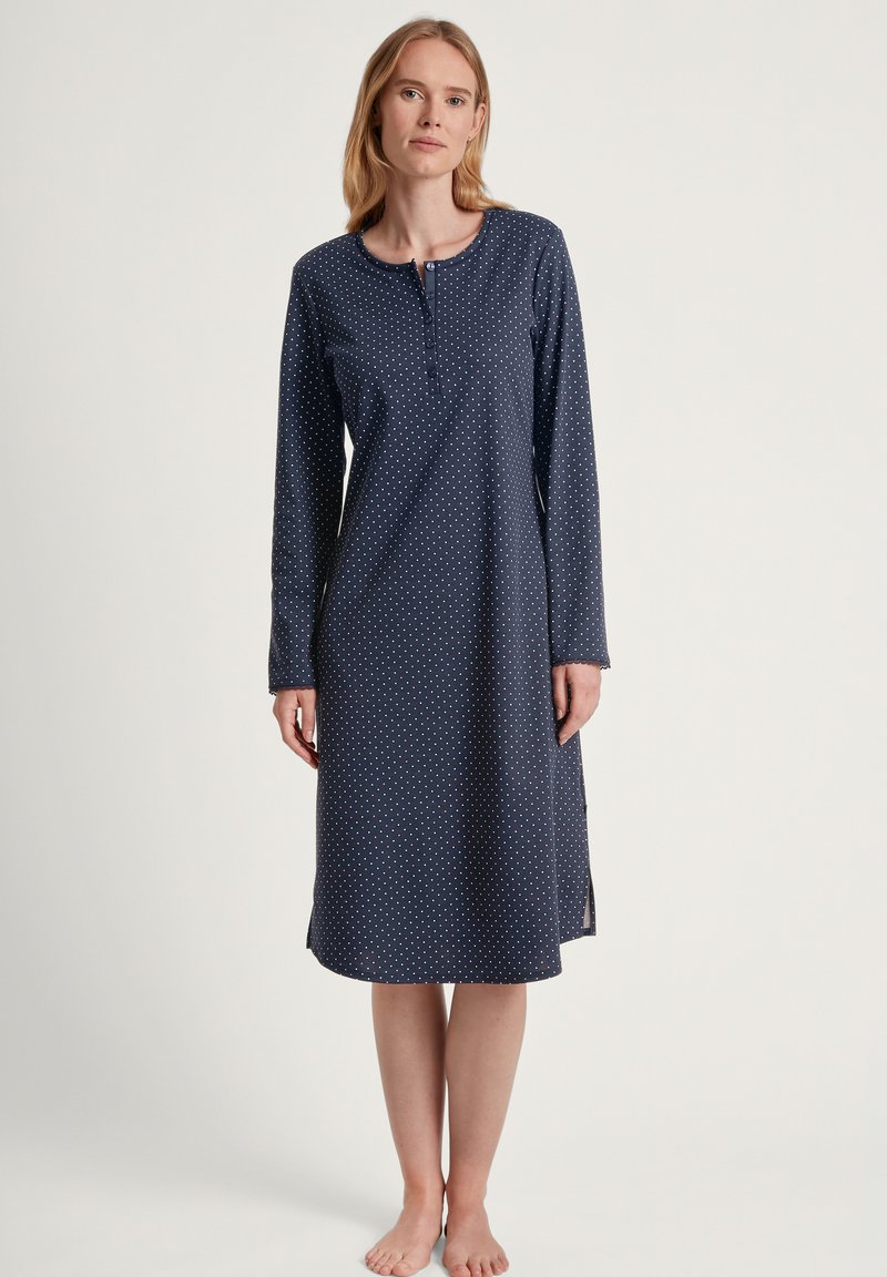 Camicione a maniche lunghe di colore blu scuro con pois bianchi. Presenta un collo rotondo e una fila di bottoni. Tessuto morbido con fessure laterali.