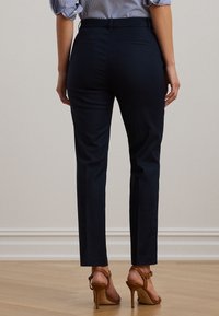 Tamsiai mėlynos, liesos formos siuvinėtos kelnės su lygiu audiniu ir vidutinio aukščio liemeniu. Yra užpakalinės kišenės ir siaurėjanti kojų forma.