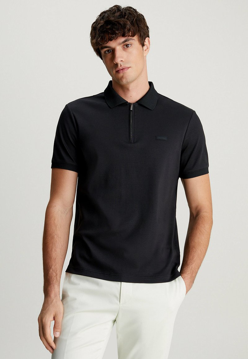 Zwarte poloshirt met een ritskraag, korte mouwen en een slim fit. Kenmerkt zich door een subtiele logo op de borst en een gladde textuur.