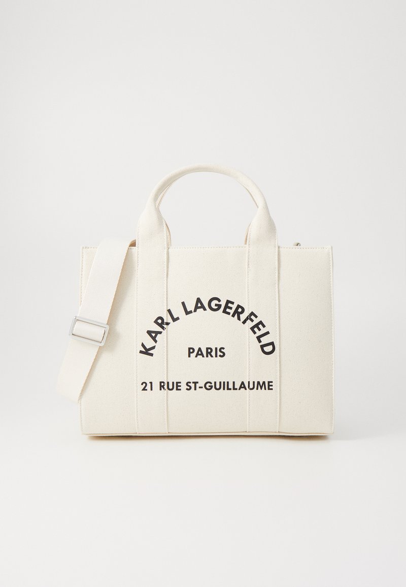 Sac à main en toile blanche avec deux poignées supérieures et une sangle réglable. Le texte imprimé en noir indique "KARL LAGERFELD PARIS 21 RUE ST-GUILLAUME."