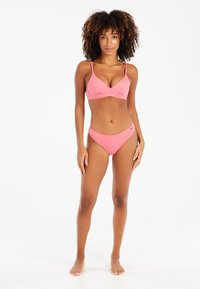 Pink ribbelbikini mit dreieckigem Oberteil, dünnen Trägern und tief sitzenden Höschen. Glatte Textur mit minimalem Hardware-Zubehör.
