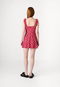 Punainen kukkamekko, jossa on neliönmuotoinen selkä, rypytetyt hihnat ja tiukka bodice, joka levenee lyhyeksi hameeksi. Yhdistetty mustiin sandaaleihin.