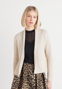 Beige stripete cardigan med åpen front, parret med en svart topp og et leopardmønstret skjørt. Glatt tekstur, tettsittende silhuett.