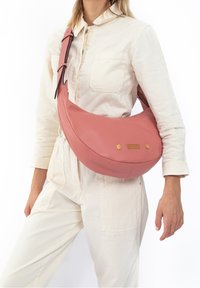 Pink leather hobo bag with a curved shape, adjustable strap, and gold hardware accents. Features a textured surface and mesh detail.
