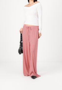 Bílý top s odhalenými rameny a dlouhými rukávy ve spojení s kalhotami s širokými nohavicemi v červené a bílé pruhované barvě. K outfitu patří černá kabelka a černá obuv.