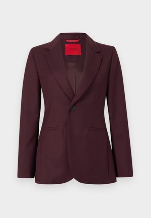 Bordeauxroter Blazer mit Reverskragen, Ein-Knopf-Verschluss, zwei Vorderentaschen und dezent strukturierter Stoff. Das Innenfutter zeigt ein rotes Etikett.