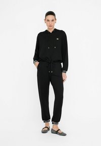 Čierny loungewear set s kapucňou a sťahovacími šnúrkami, v súprave so zodpovedajúcimi priliehavými nohavicami s elastickými manžetami.