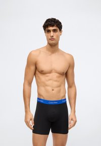 Svarta bomullsboxershorts med ett blått elastiskt midjeband med "Calvin Klein"-logotyp. Tyget ser slätt och figursytt ut, designat för komfort.