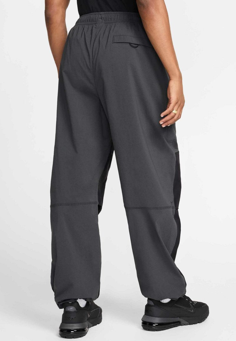 Pantalones deportivos grises con un corte relajado, cinturilla elástica, bolsillos laterales y detalle de panel en contraste en negro. Llevados con zapatillas negras.