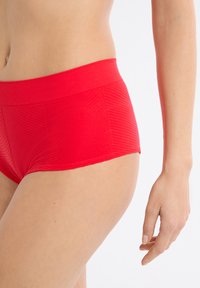 Slip rosso con motivo a costine orizzontali testurizzate, ampia fascia elastica in vita e taglio semplice. Il materiale sembra morbido ed elastico.