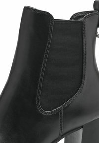 Bottine en cuir noir avec empiècement latéral élastique et talon bloc, coutures détaillées et languette à l'arrière.