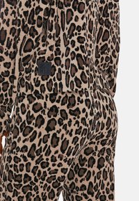 Komplet odzieży domowej w zwierzęcy wzór, w odcieniach beżu i brązu, charakteryzujący się miękką teksturą oraz czarną metką marki z tyłu.