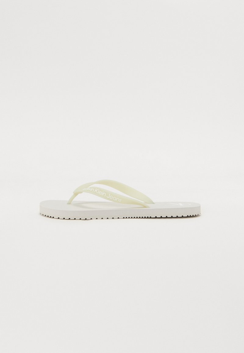 Hvite flip-flops med lysegule stropper, med en teksturert såle og trykket merkenavn på stroppen. Enkelt design og flat profil.