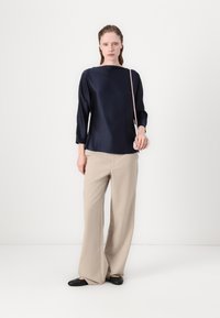Marineblå satengtopp med trekvartssømmer, kombinert med beige vide bukser og svarte flate sko. Minimalistisk design med et rent silhuett.