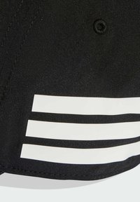 Gorra negra con tres rayas horizontales blancas en la visera. Tela lisa con un brillo sutil, diseño estructurado y detalles cosidos.