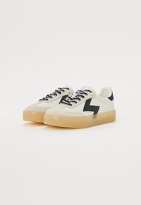Hvite sneakers med svarte detaljer, med en overdel av semsket skinn og syntetisk materiale, tykk gjennomsiktig såle, og svarte og hvite snørebånd.