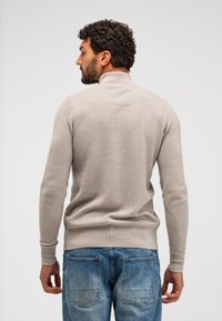 Beiger gestrickter Pullover mit hohem Kragen, strukturiertem Muster und gerippten Bündchen und Saum. Getragen mit hellblauen Jeans.
