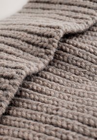 Tessuto lavorato a maglia beige con motivo a coste strutturato, che mostra bordi piegati e un aspetto morbido e peloso.