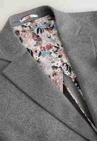 Grauer Blazer aus strukturiertem Stoff. Das Innenfutter zeigt ein florales Muster in Pink, Blau und Schwarz auf hellem Hintergrund.