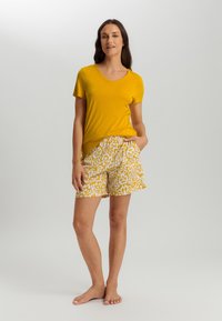 Geel V-hals T-shirt gecombineerd met gele en witte shorts met patroon. De shorts hebben een abstract ontwerp en zijzakken.