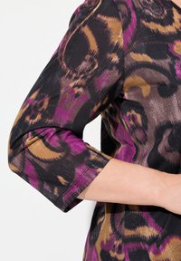 Langsleeve top met een zwart, paars en bruin bloemenpatroon. De stof lijkt gestructureerd; de mouwen zijn iets omgeslagen.