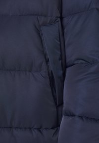 Mørkeblå pufferjakke med en glat, blank tekstur, der har vandrette quiltede sektioner og en sidelomme med en skjult flap.