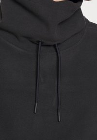 Sudadera con capucha negra de forro polar, con un cuello alto, que cuenta con cordones ajustables y una superficie texturizada. La vista en primer plano destaca el material y el diseño.