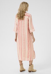 Rochie lungă, cu un model complex în roz deschis, decorată cu designuri geometrice intricate. Dispune de mâneci trei sferturi și fante laterale, fiind asortată cu cizme bej până la glezne.