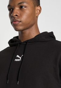 Felpa nera con cappuccio in cotone dal tocco morbido, caratterizzata da un logo Puma bianco sul petto e da un cordino regolabile al collo.