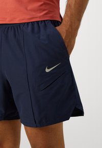 Navy blue athletic shorts with an elastic waistband, featuring a sleek Nike logo and zippered side pockets for storage. Lightweight material.