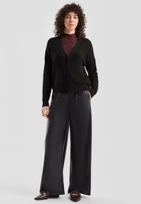 Czarny dziergany kardigan z trzema guzikami, noszony na bordowej bluzce z długim rękawem. Połączony z luźnymi czarnymi spodniami i ciemnymi butami.